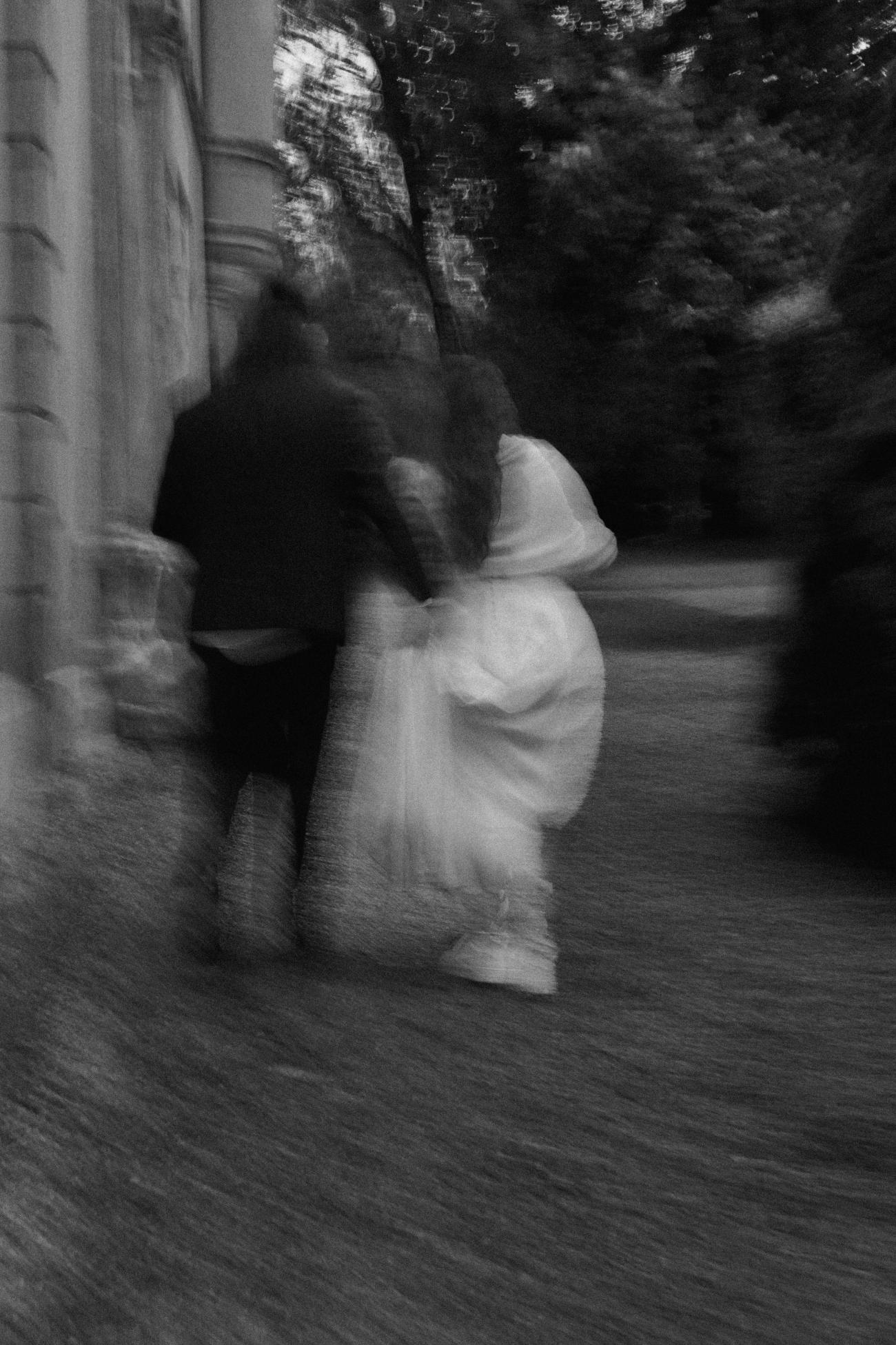 Photo floue avec du grain, en noir et blanc d'un couple de mariés qui marche. La photo est très artistique et invite à la rêverie.